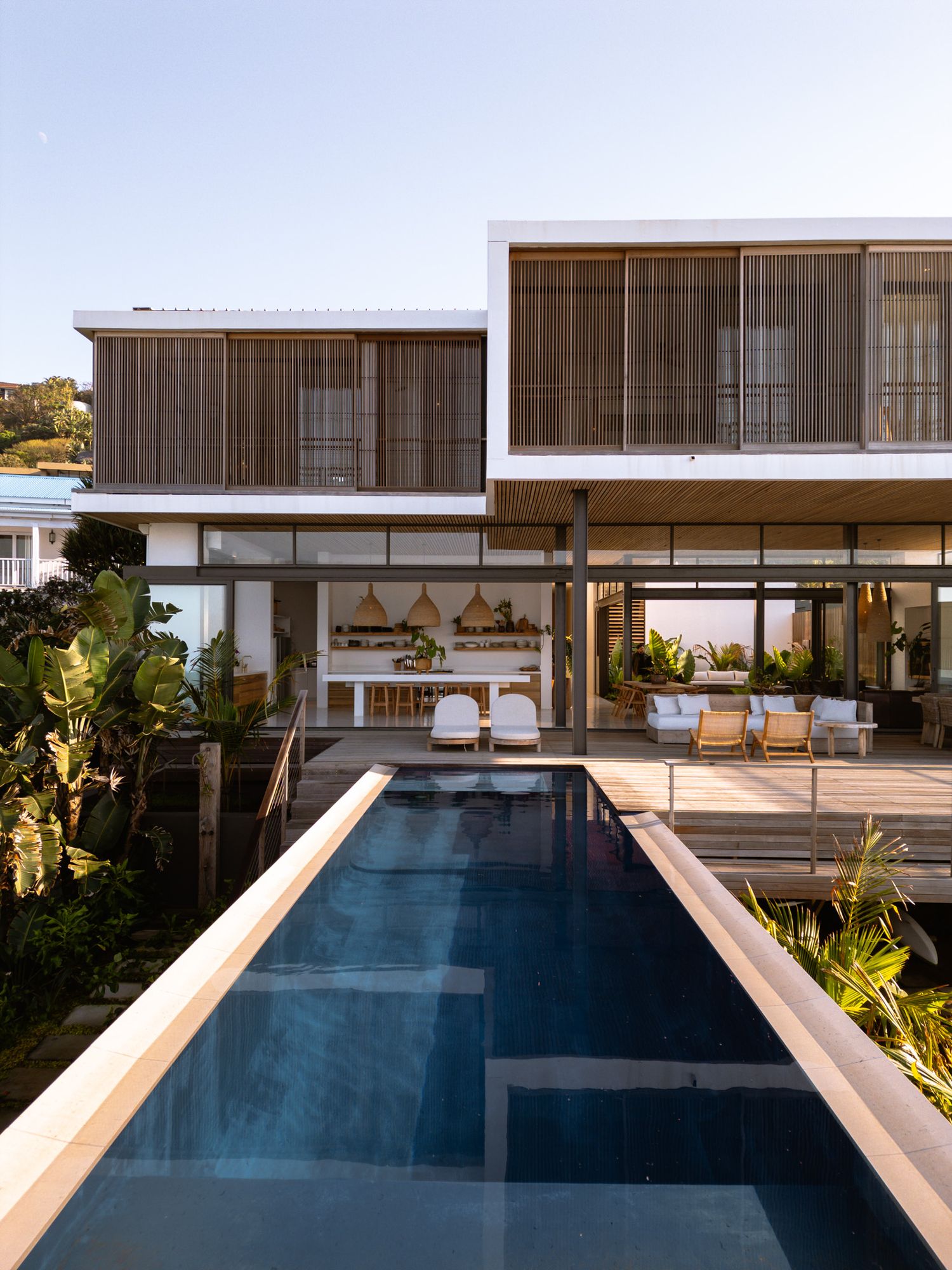 Sleek modern house with infinity pool and wooden deck overlooking coastal view.