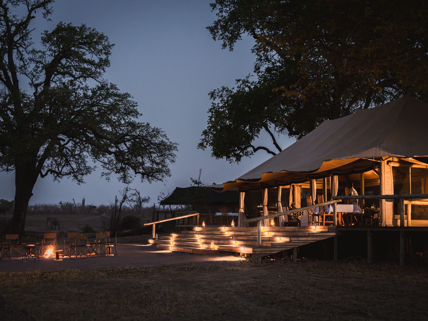 Safari lodge illuminated at dusk with lantern-lit pathways leading to main building.