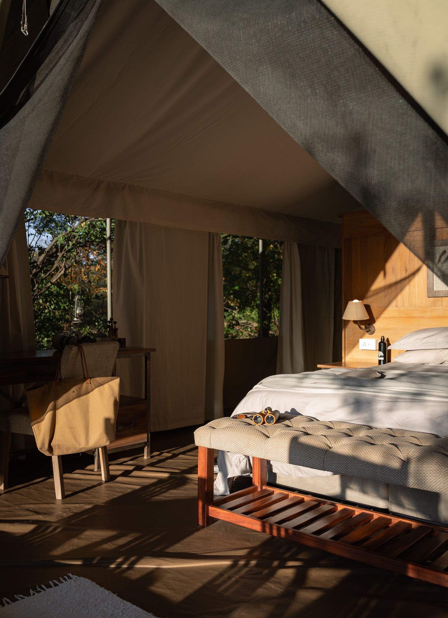 Luxurious safari tent interior with comfortable bed and wooden furniture bathed in natural sunlight.