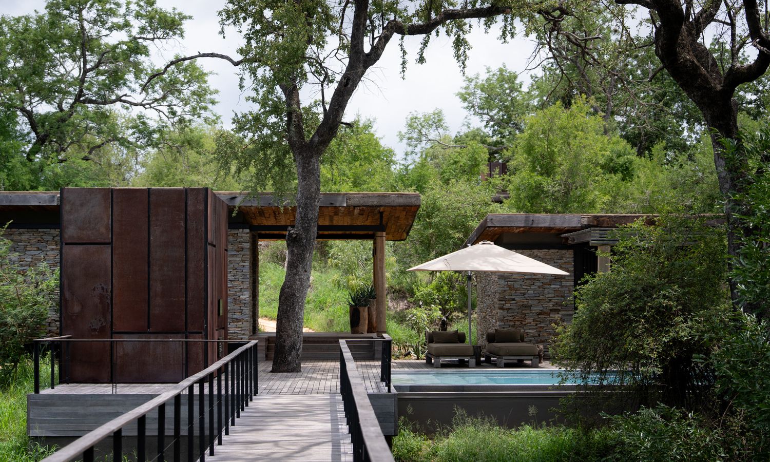 Elevated wooden deck walkway surrounded by trees and natural landscaping at a luxury safari lodge.