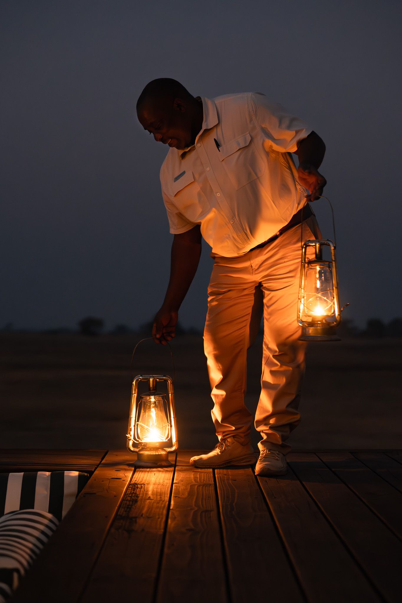 Staff member setting up lanterns on wooden deck at twilight.