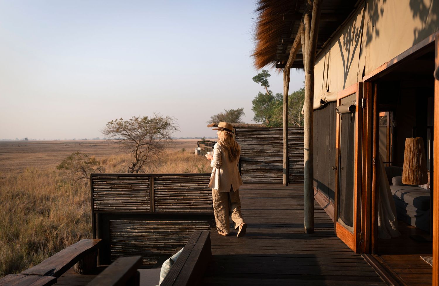 Person standing on a safari lodge deck overlooking vast African savanna plains at golden hour.