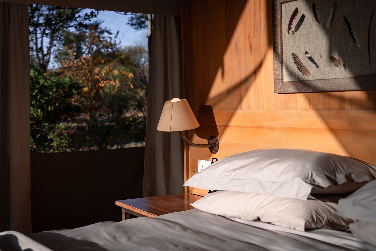 Sunlight streams through windows into a cozy bedroom with natural wood furnishings and white bedding.