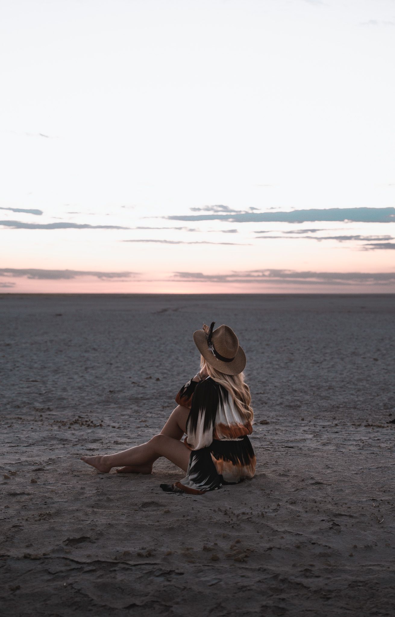 A contemplative moment on desert sands during a pastel sunset.