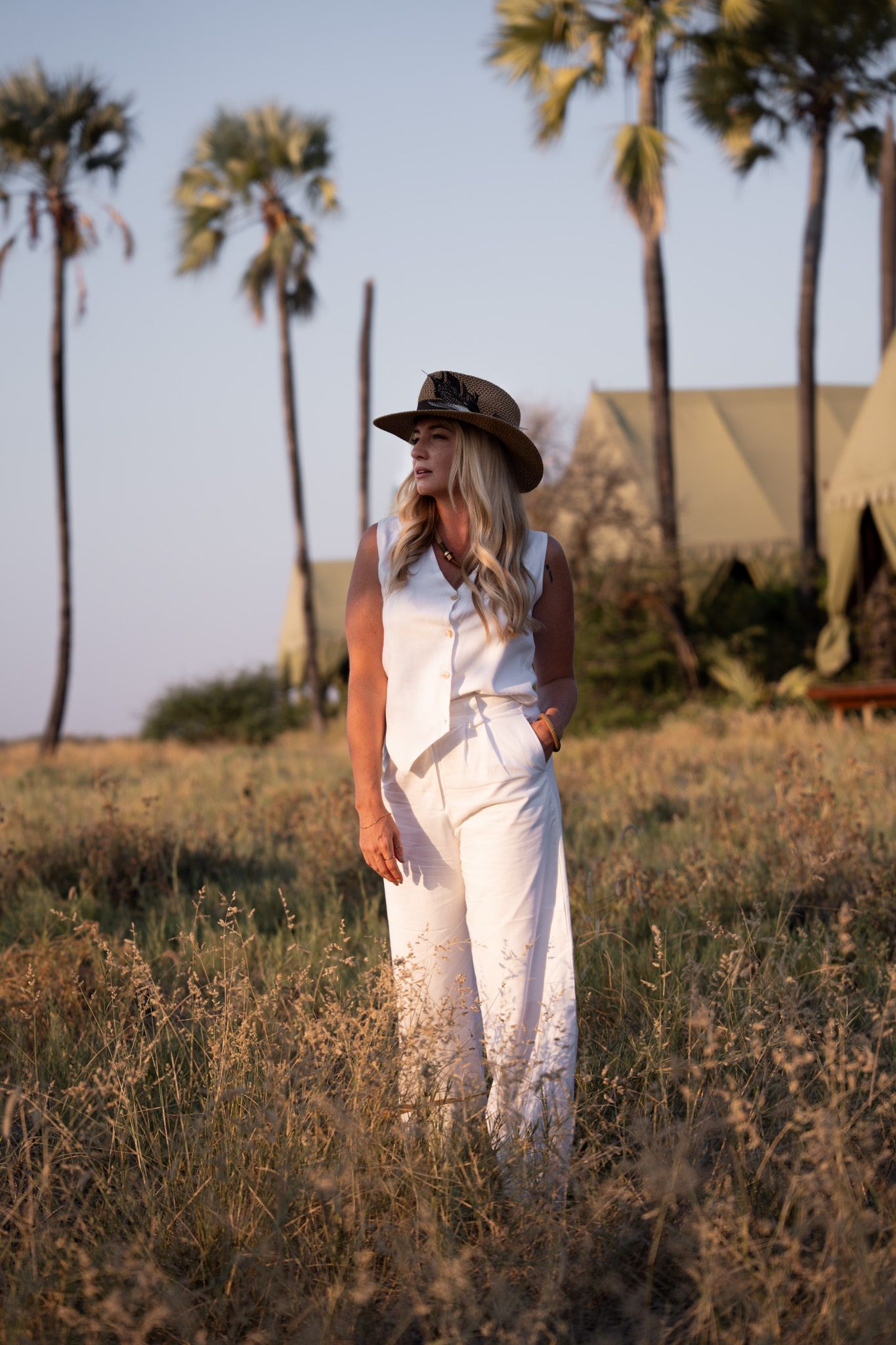 Palm trees line a grassy field during golden hour with a person walking in white clothing.