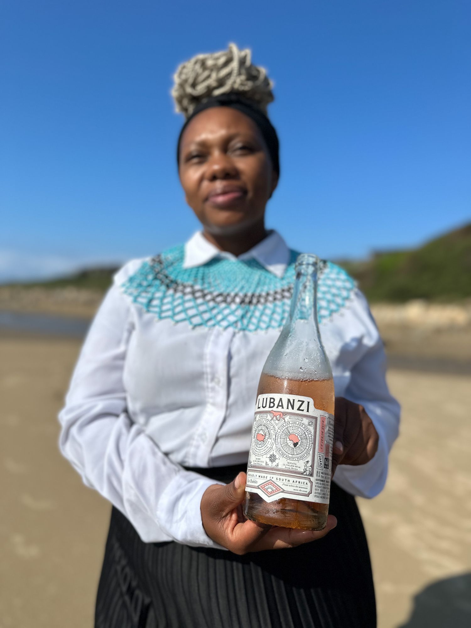 Traditional African attire worn while presenting Ubanzi branded bottle against coastal backdrop.