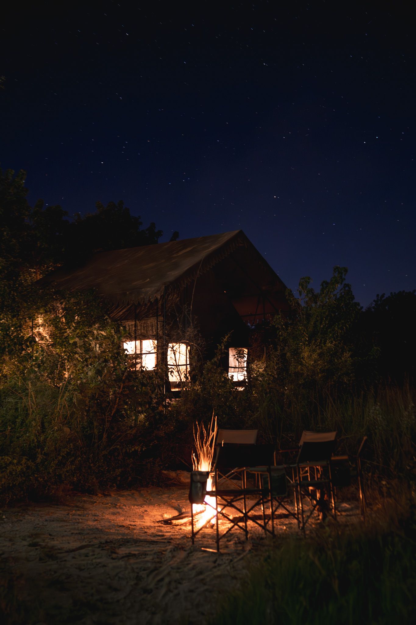 Nighttime view of illuminated safari tents with campfire creating a cozy wilderness atmosphere.
