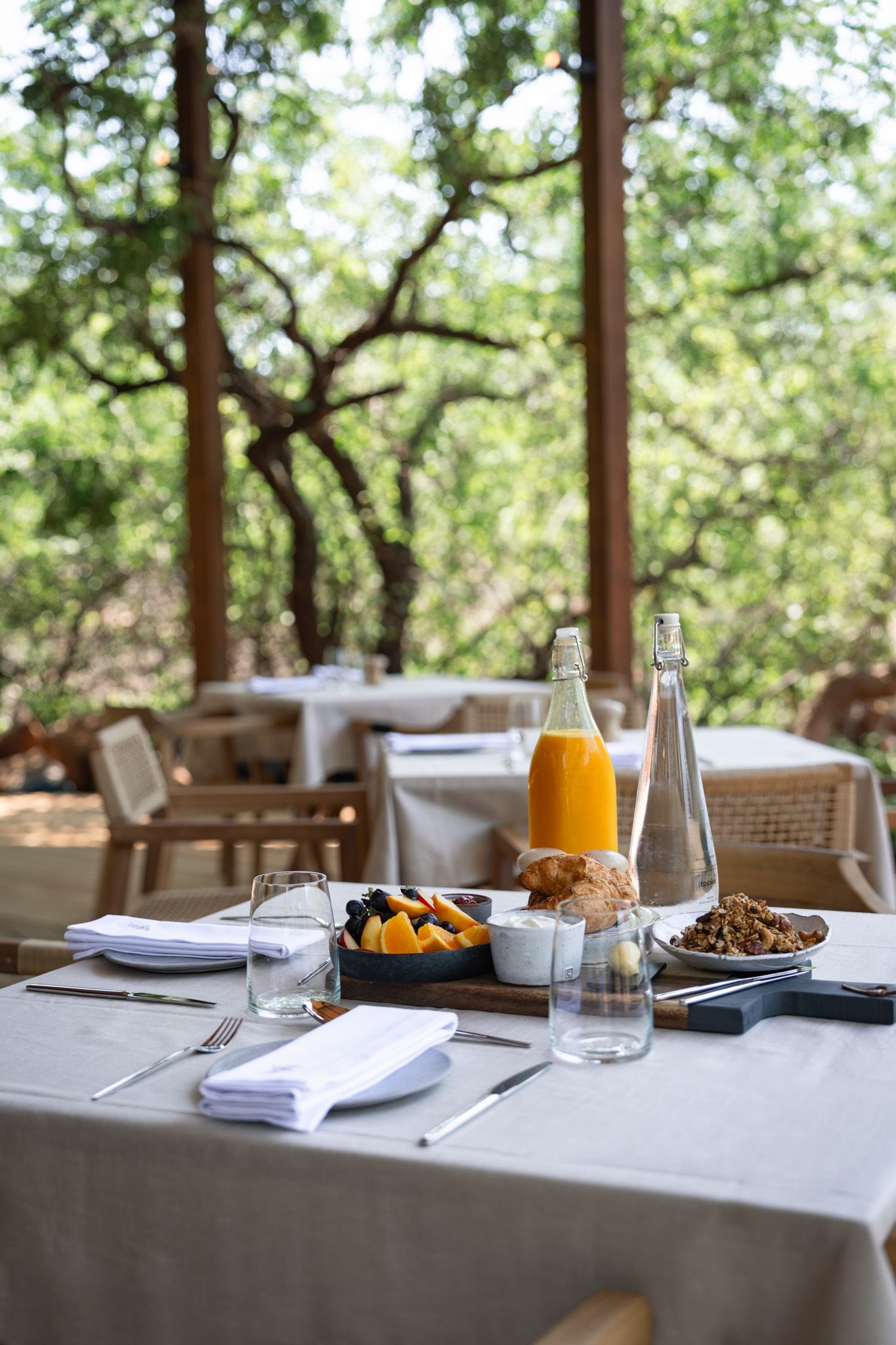 Elegant breakfast table setting with orange juice and fresh fruits in outdoor restaurant.