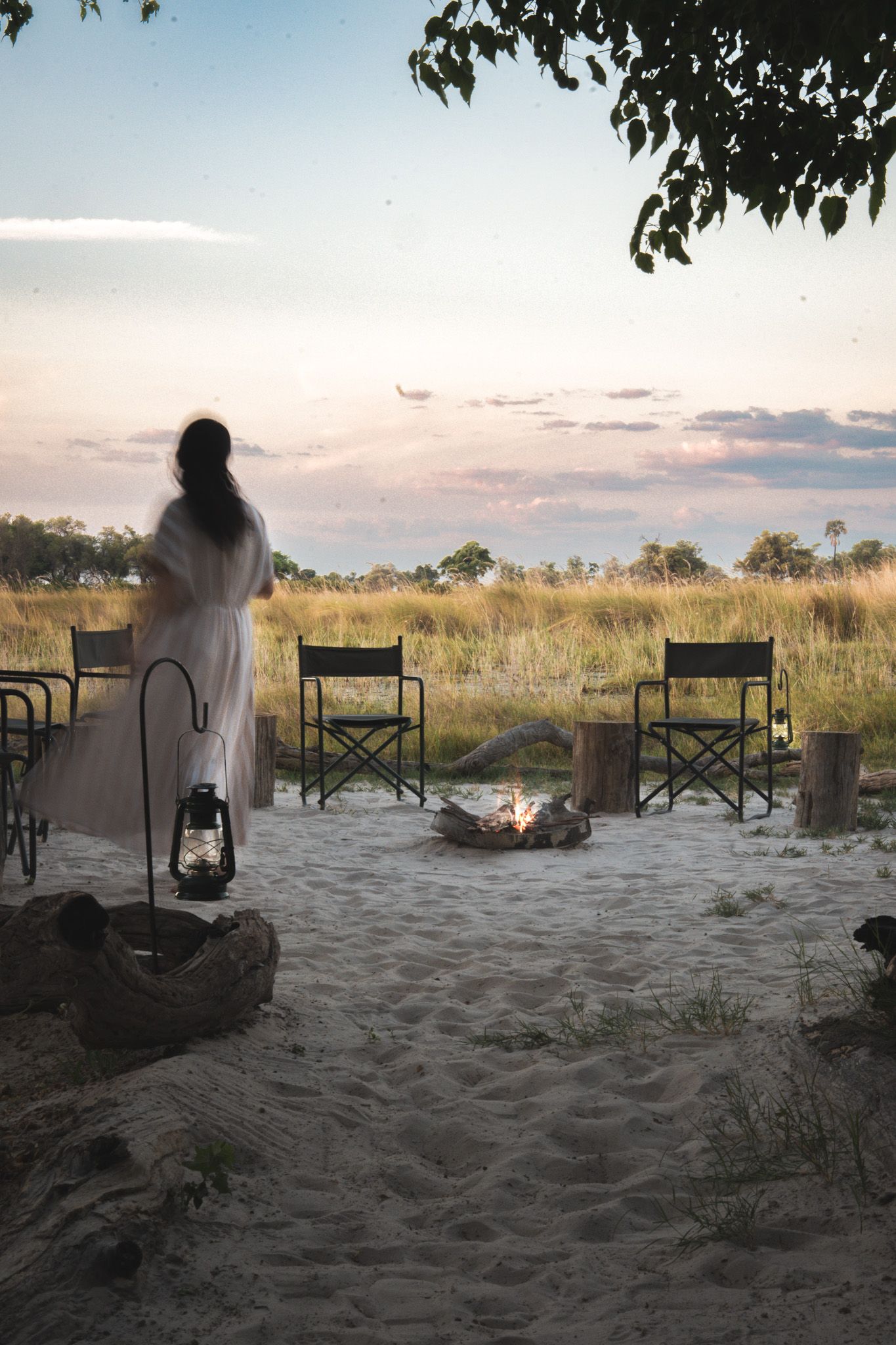 Silhouetted figures seated on beach chairs watching sunset over African grasslands.