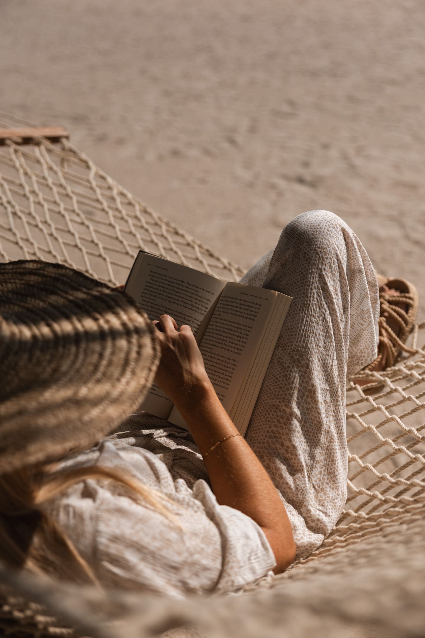 Relaxing on hammock while reading book on sandy beach.