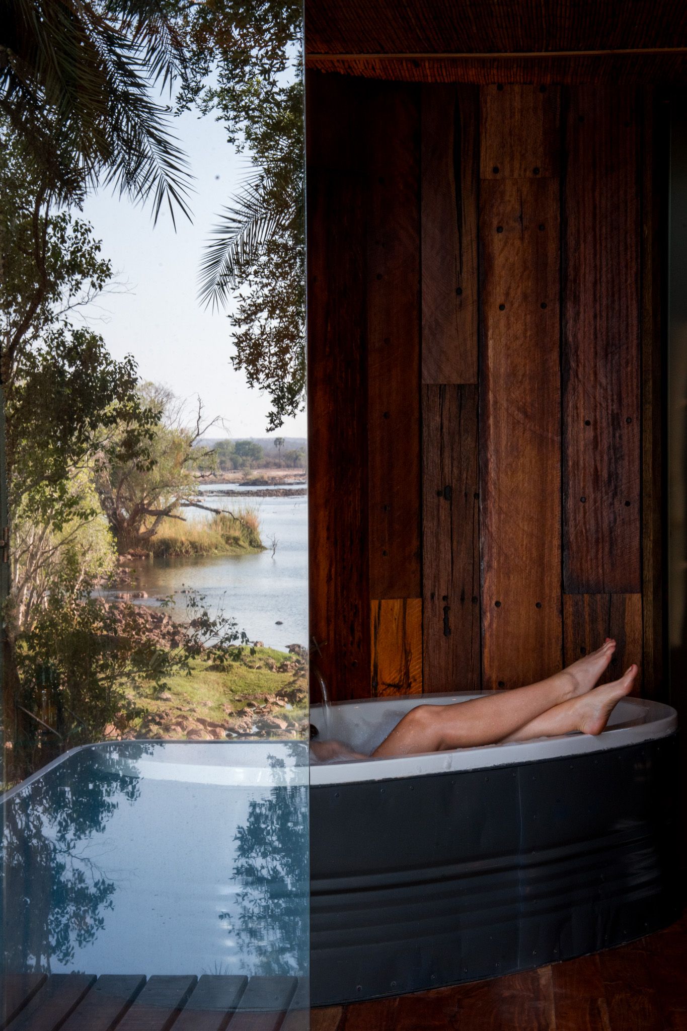 Luxurious outdoor bathtub with scenic water view through wooden architecture.