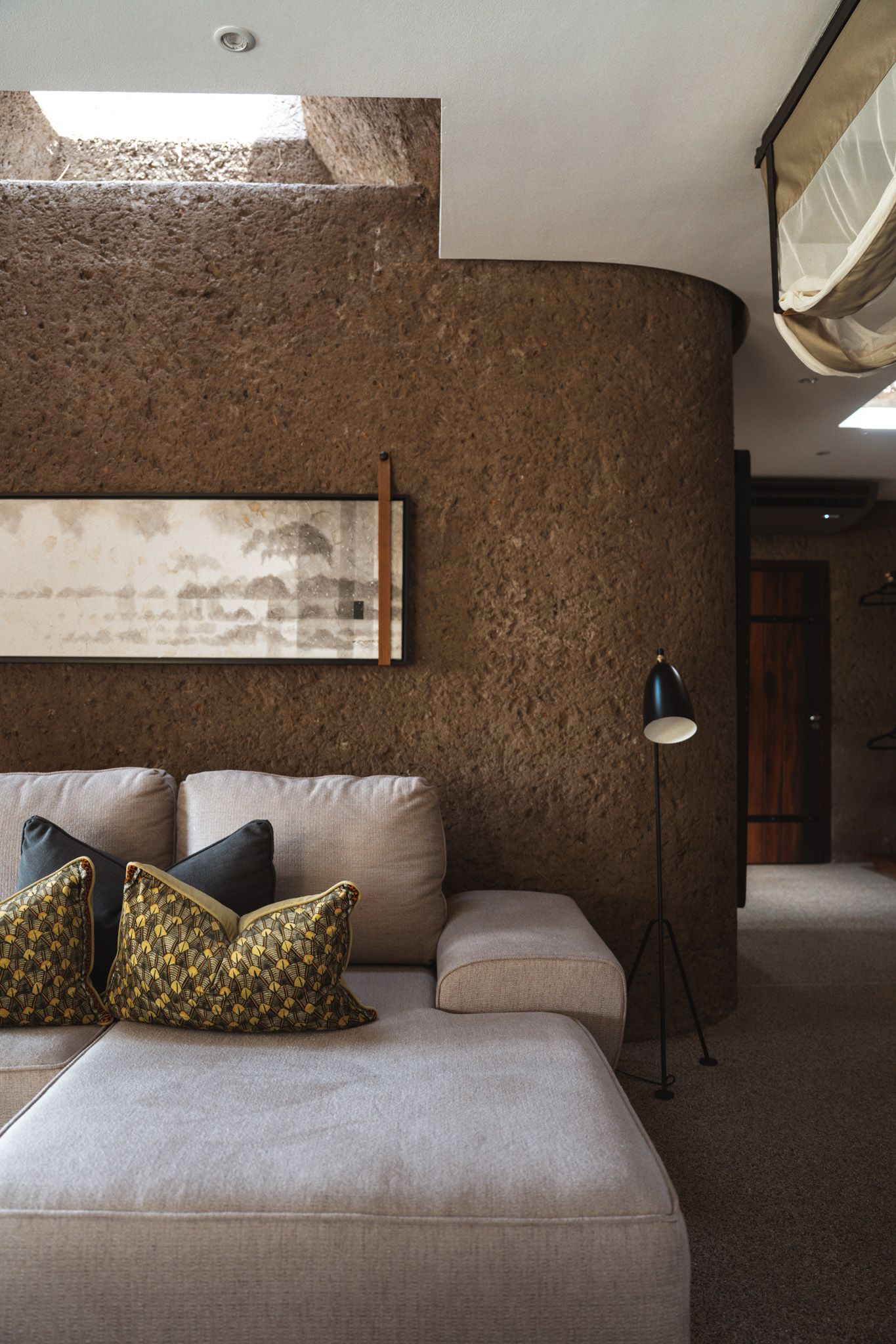Elegant living room with earth-toned walls, beige sectional sofa, and decorative pillows under skylight.