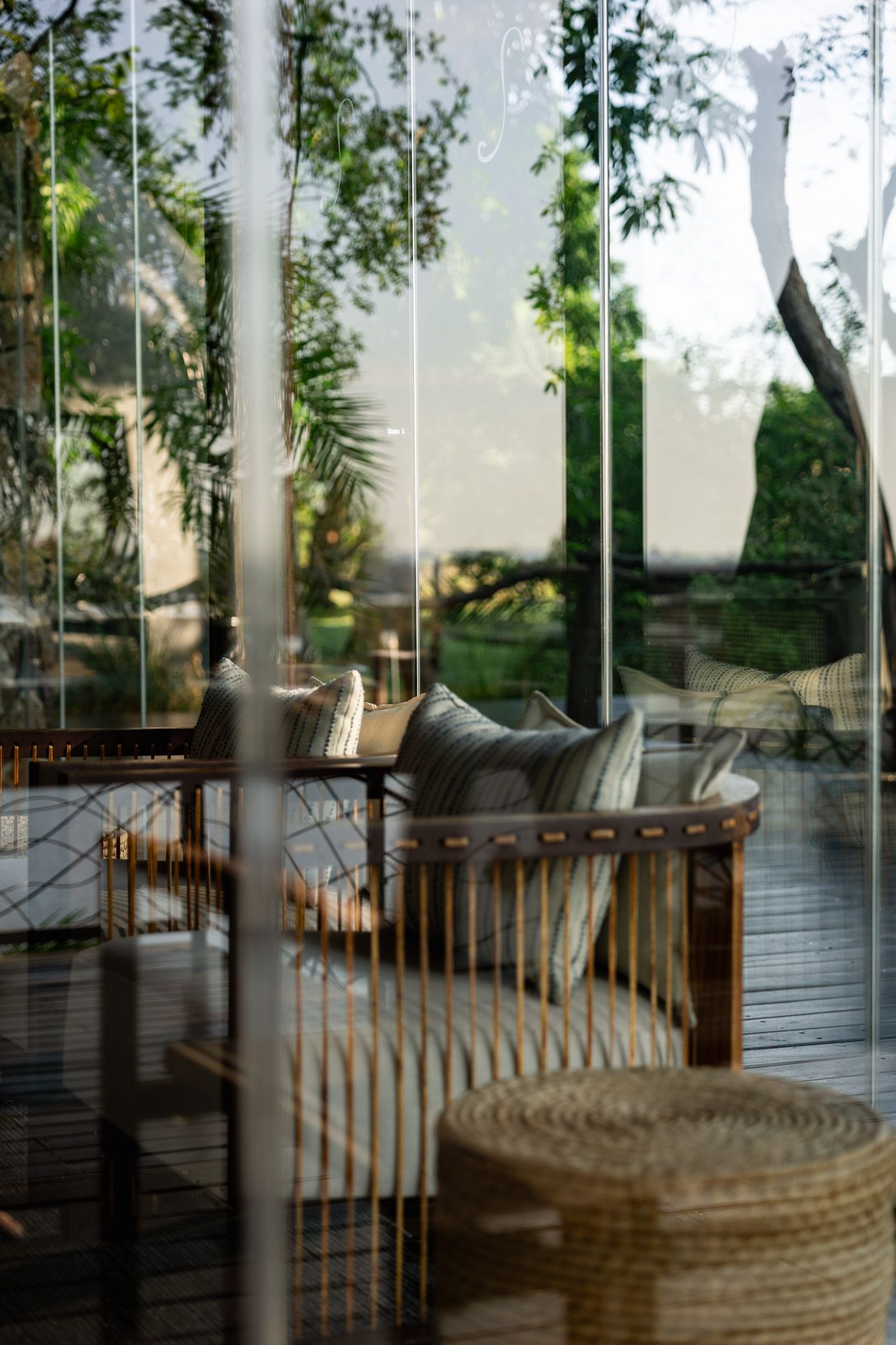 Outdoor lounge area with rattan furniture and lush greenery visible through large windows.