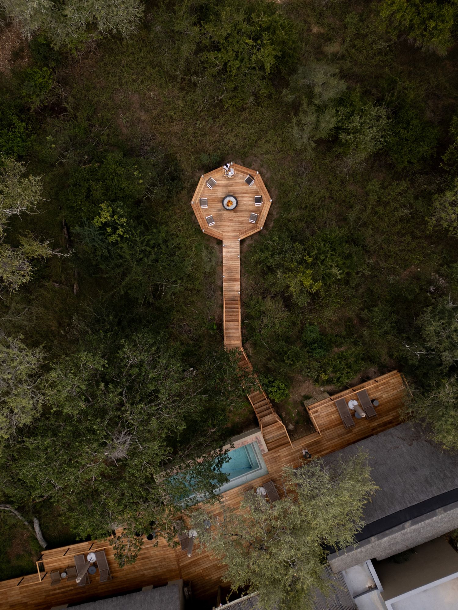 Aerial view of wooden walkways connecting to an octagonal platform with pool in forest setting.
