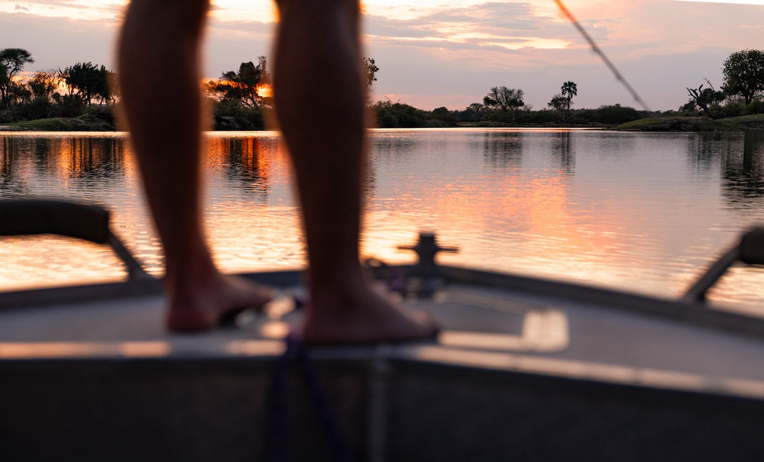 Silhouette of feet on boat during golden sunset over calm waters.