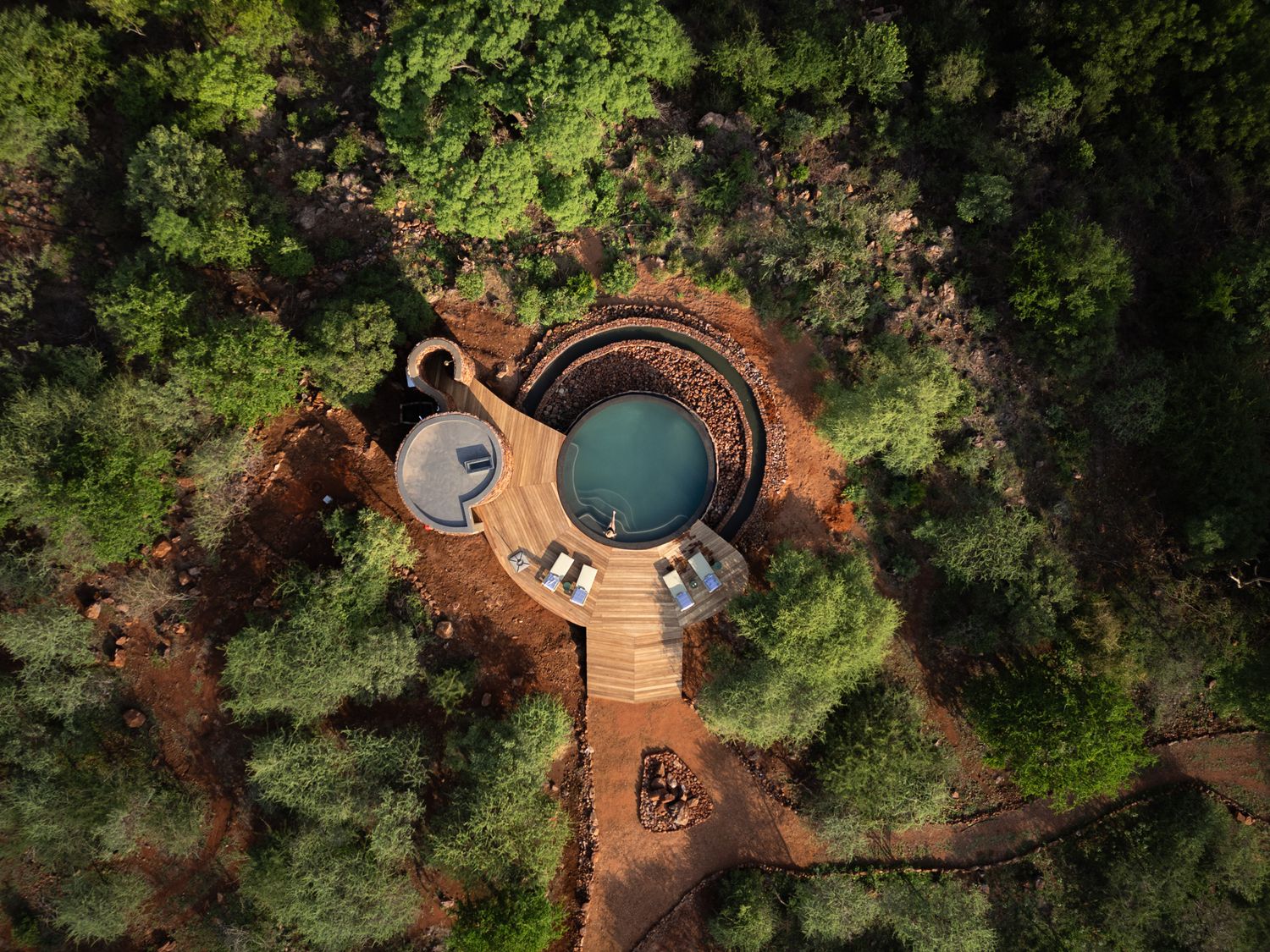 Overhead drone shot of circular pools and wooden walkways surrounded by lush forest.
