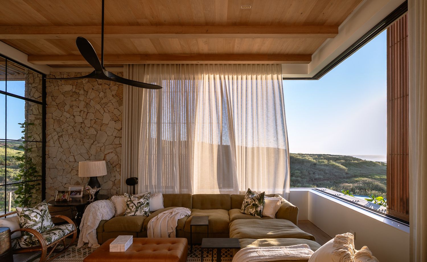 Panoramic view of modern bedroom with wooden ceiling and large windows overlooking mountain landscape.
