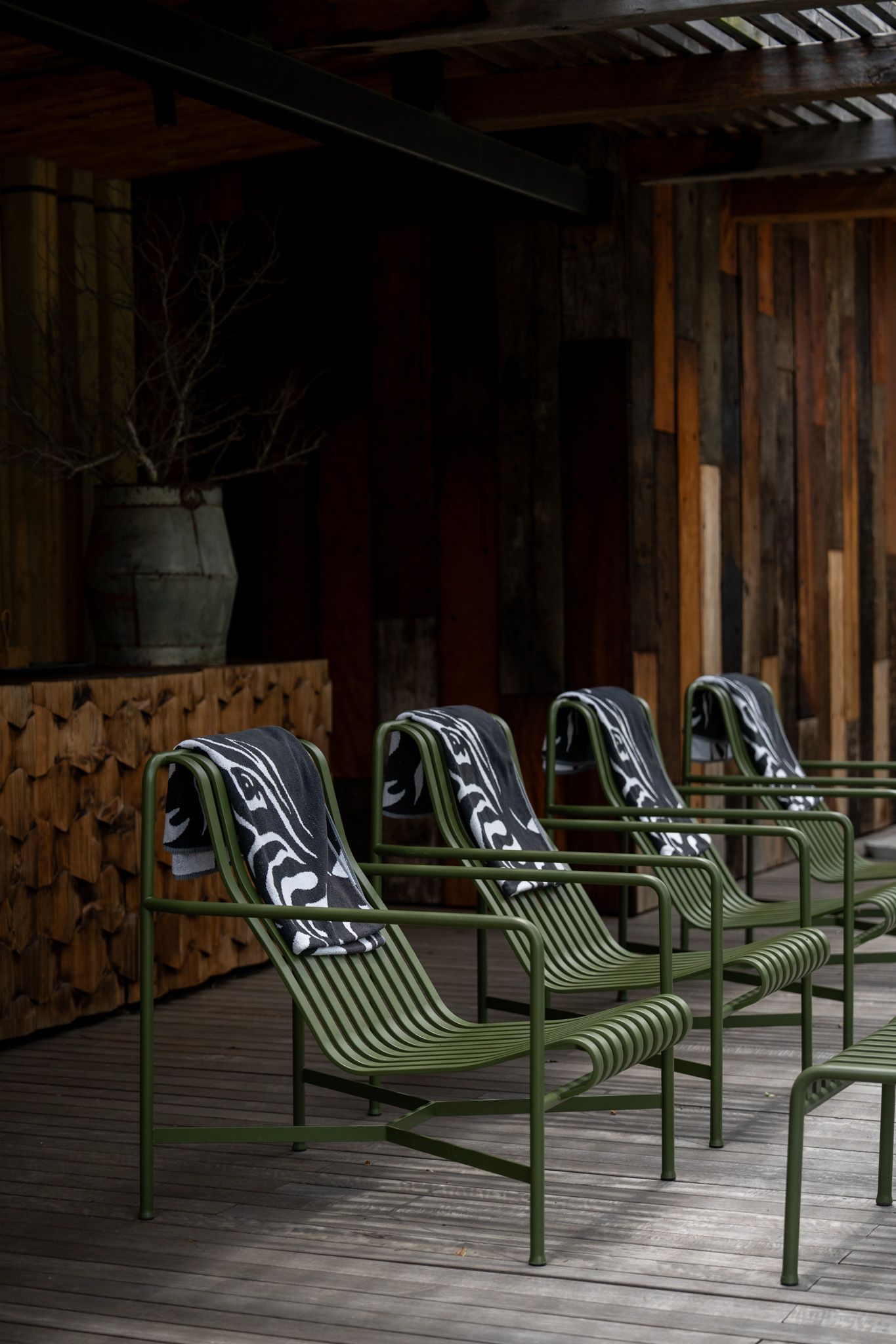 Row of minimalist green lounge chairs arranged on a wooden deck in a shaded outdoor space.