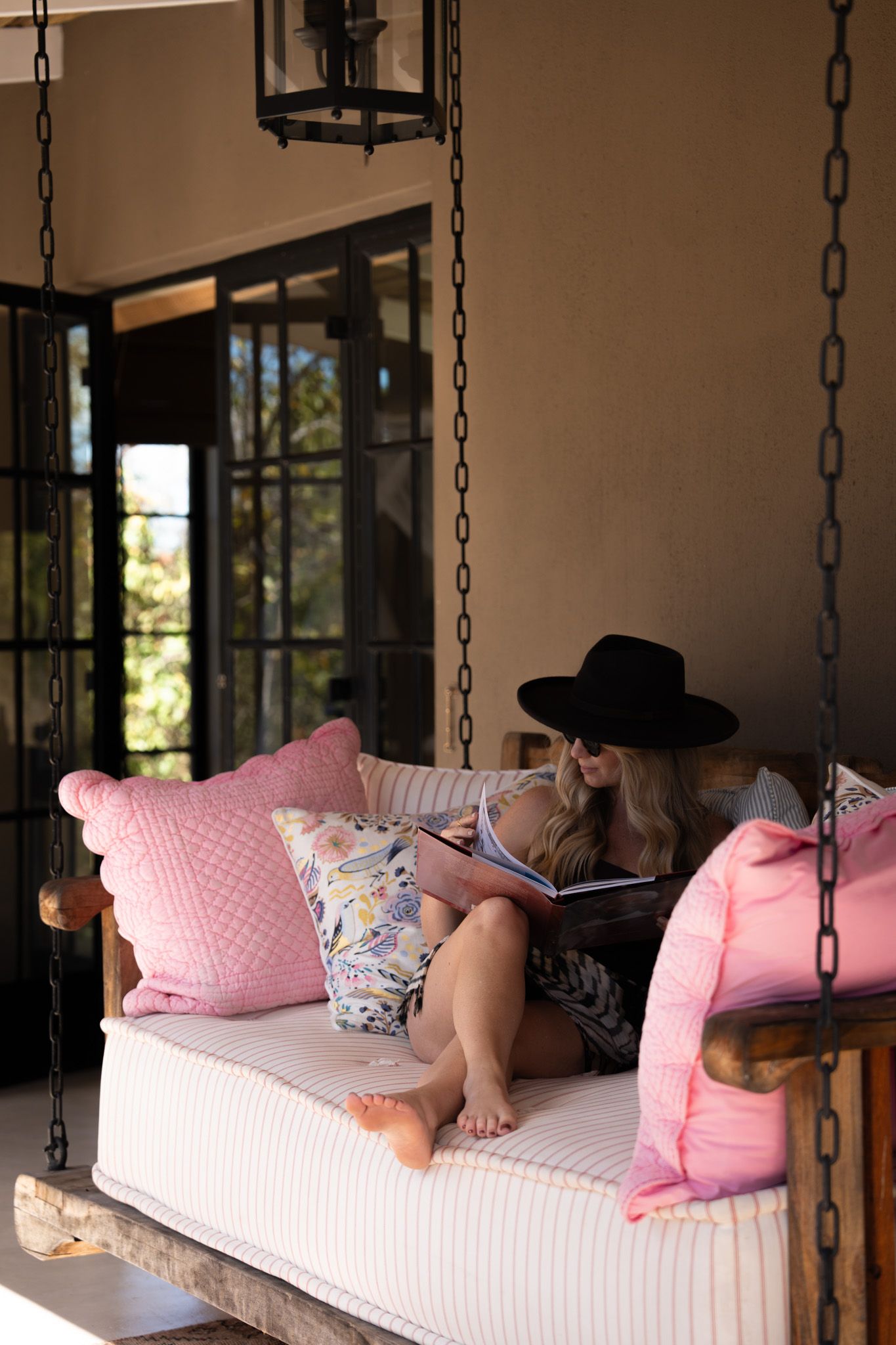 Hanging porch swing with pink pillows and cozy reading nook setup.