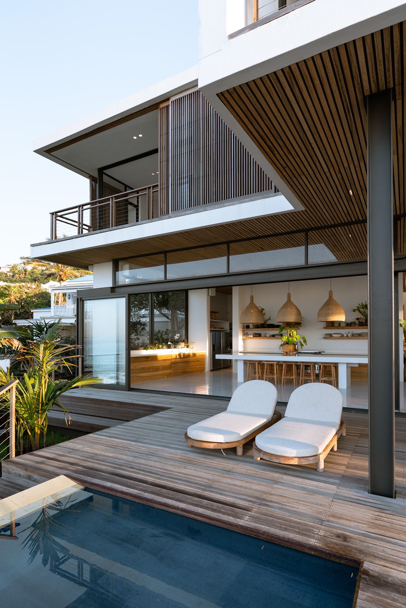 Luxurious modern house with pool deck, lounge chairs, and indoor-outdoor living space.