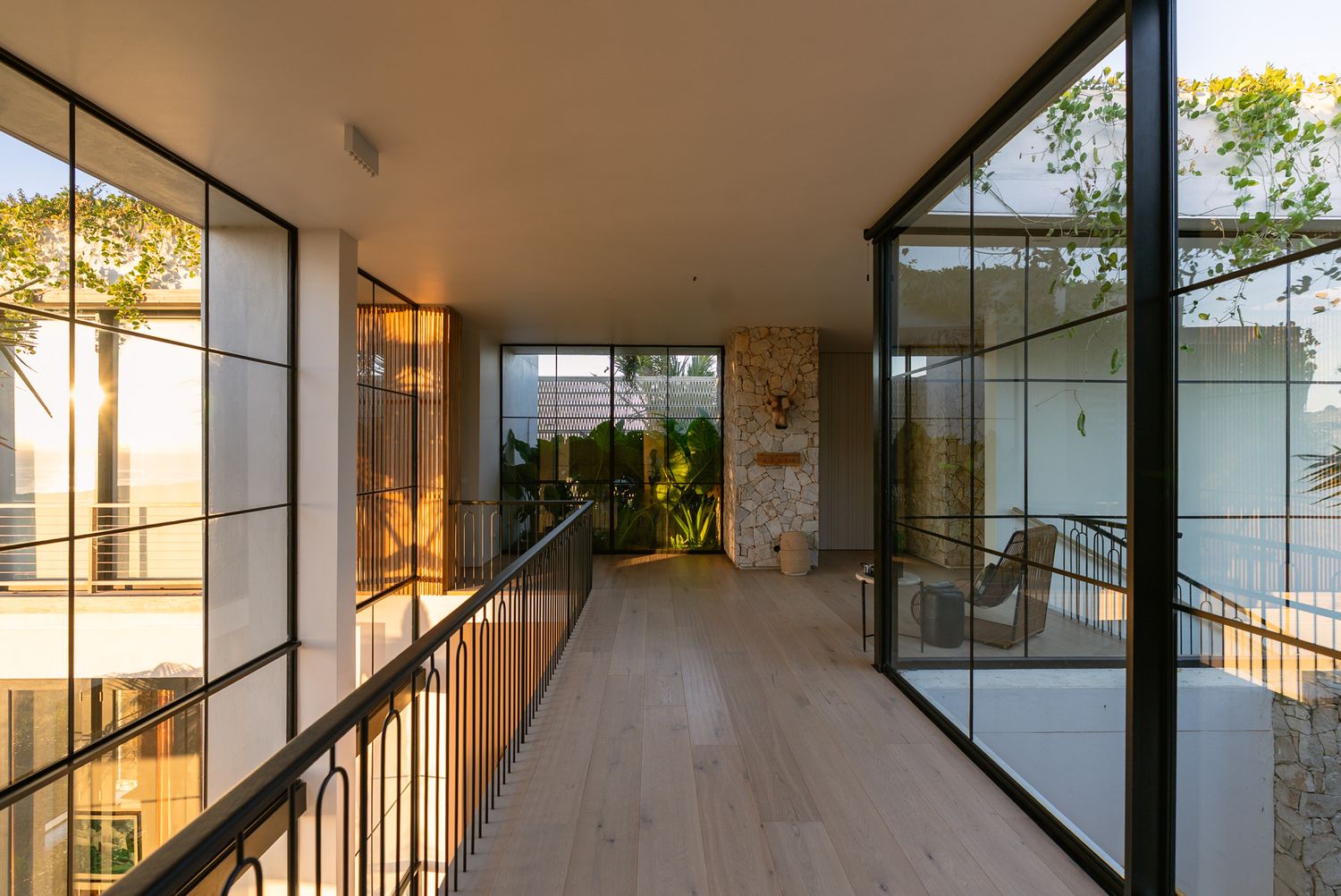 Modern hallway with floor-to-ceiling windows and wooden flooring bathed in warm sunlight.