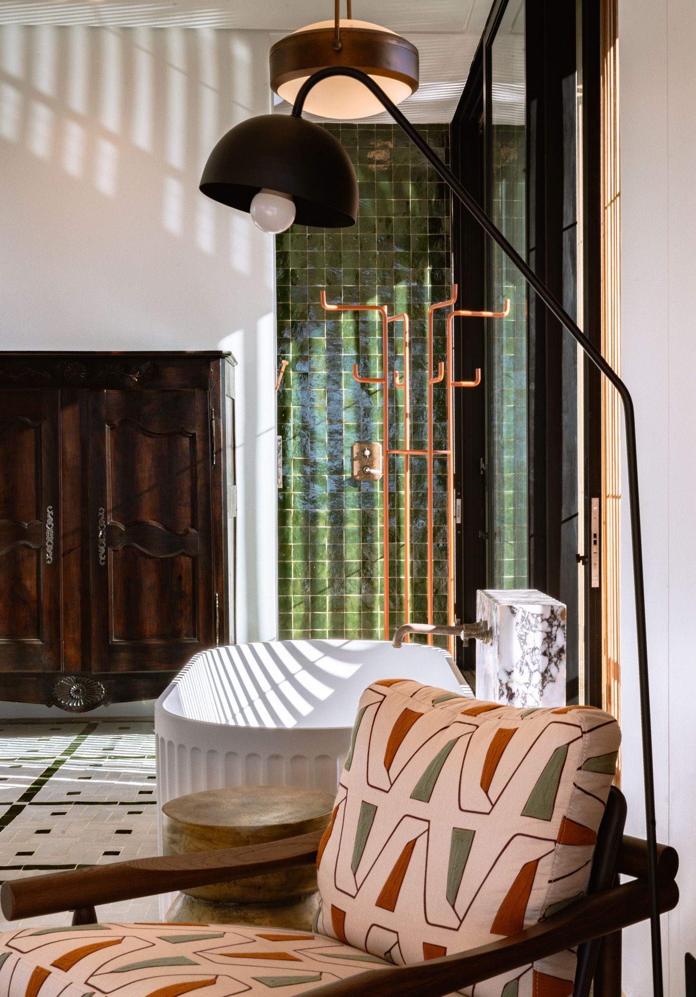 Modern interior with green tile wall, vintage wooden door, and geometric patterned chair under pendant lighting.