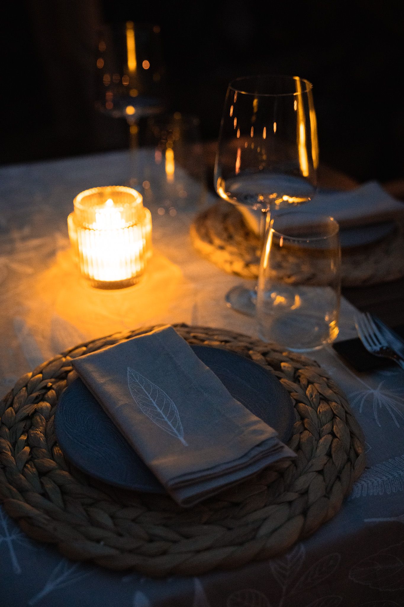 Candlelit table setting with woven placemat and wine glass creating romantic ambiance.
