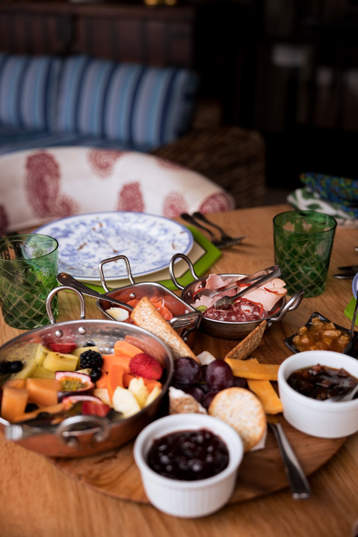 Charcuterie board with meats, cheeses, and jams served alongside green glasses on wooden table.