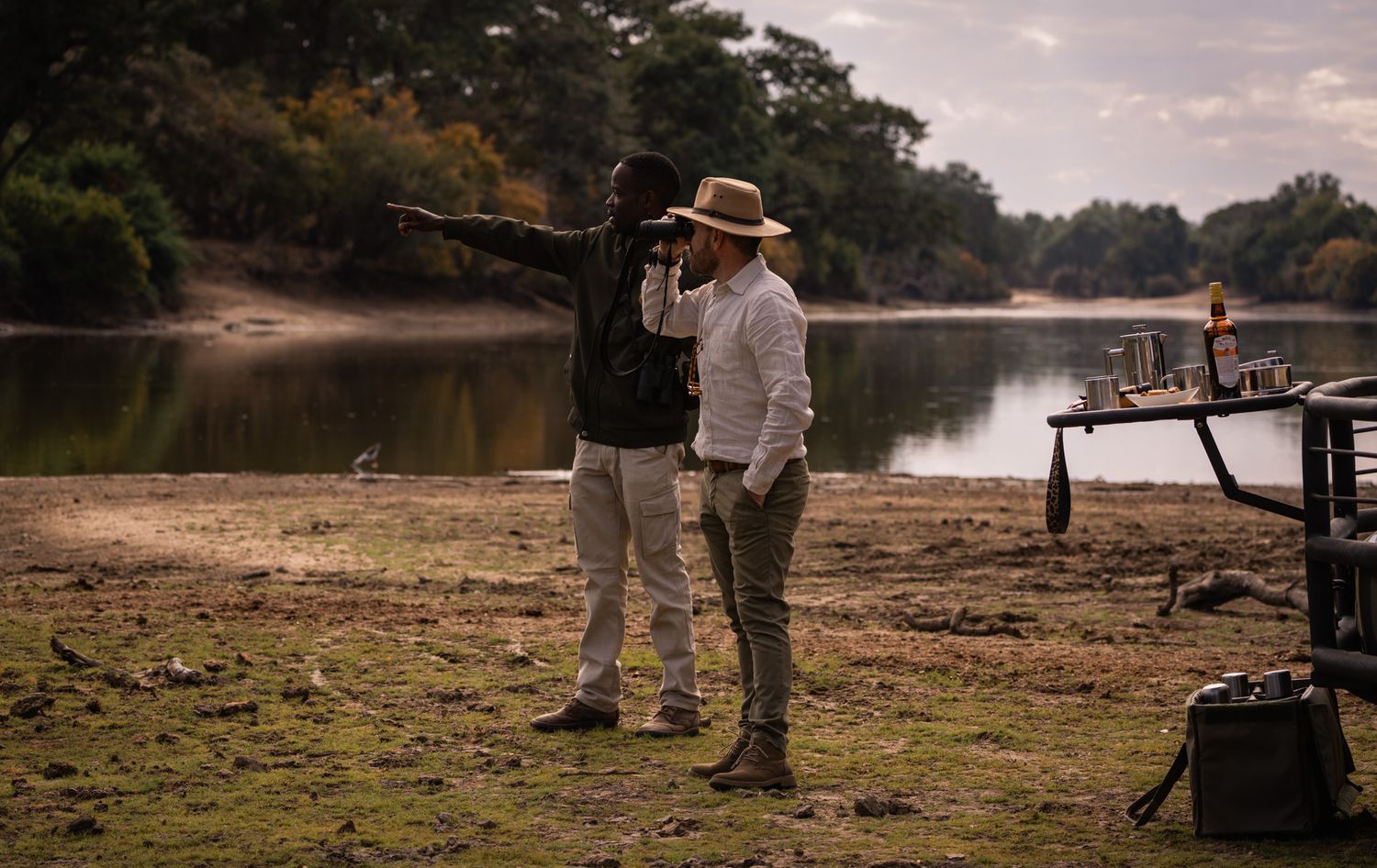 Two people observing wildlife from riverbank during safari excursion.