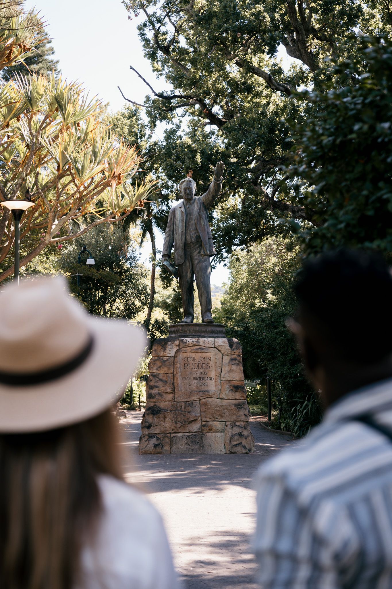 Stone monument or statue viewed through trees in a park setting.