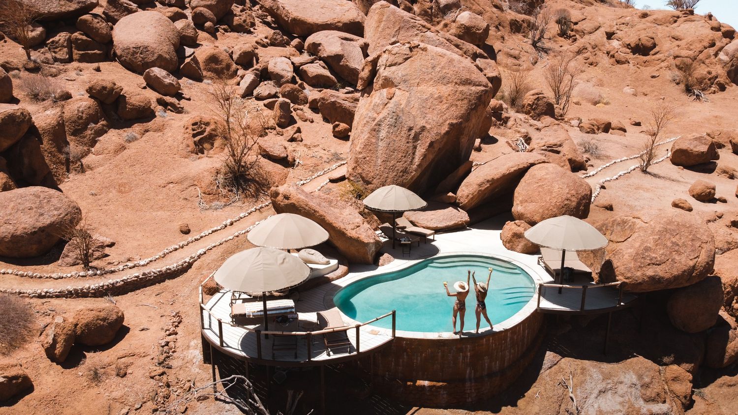 Turquoise swimming pool nestled among red rock formations in a desert landscape.