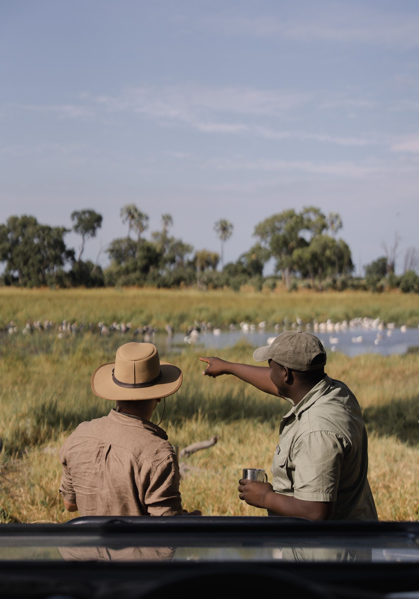 Two safari guides overlooking a waterhole filled with birds in the African savanna.