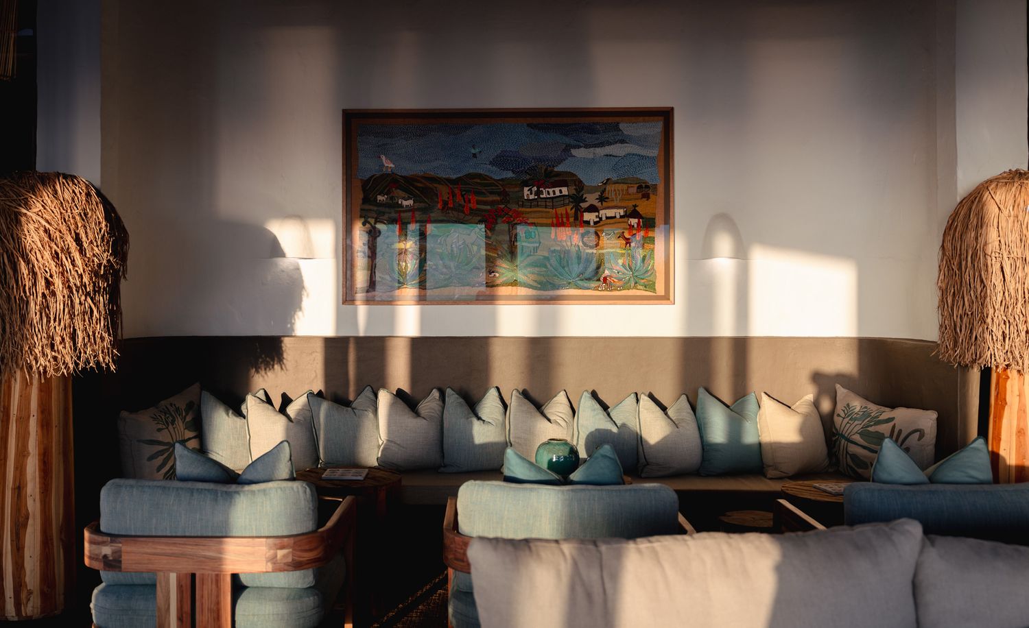 Modern lounge area with blue cushioned seating, decorative art, and natural light streaming through windows.