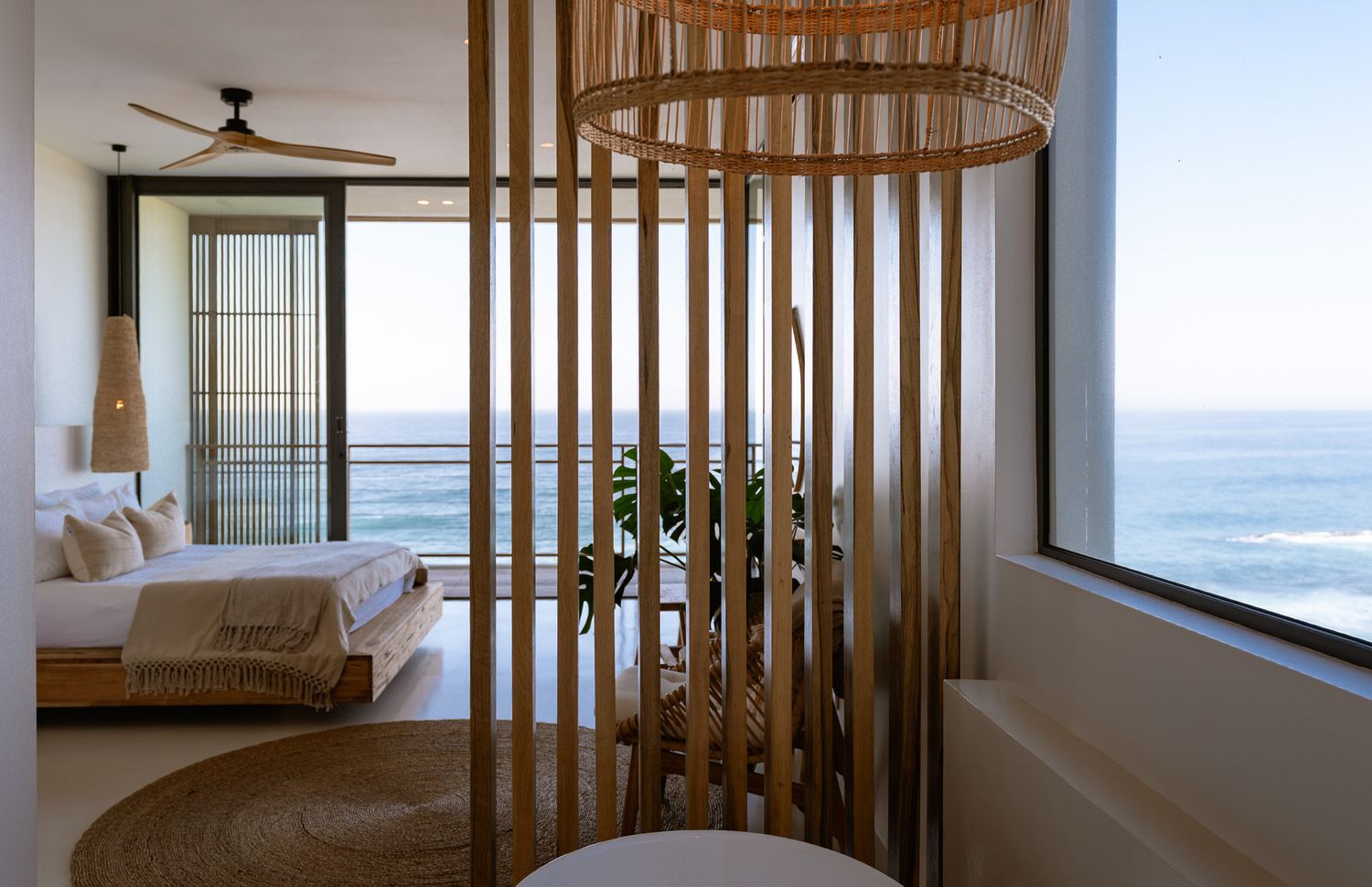 Contemporary bedroom with curved wooden slat divider and ocean view through large windows.