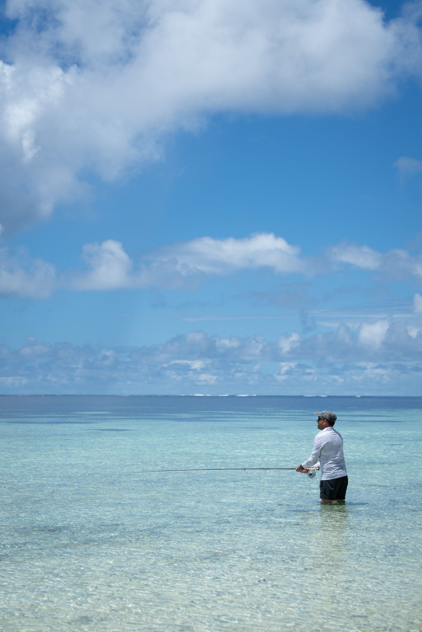 Crystal clear turquoise waters of a tropical lagoon with scattered puffy clouds in bright blue sky.