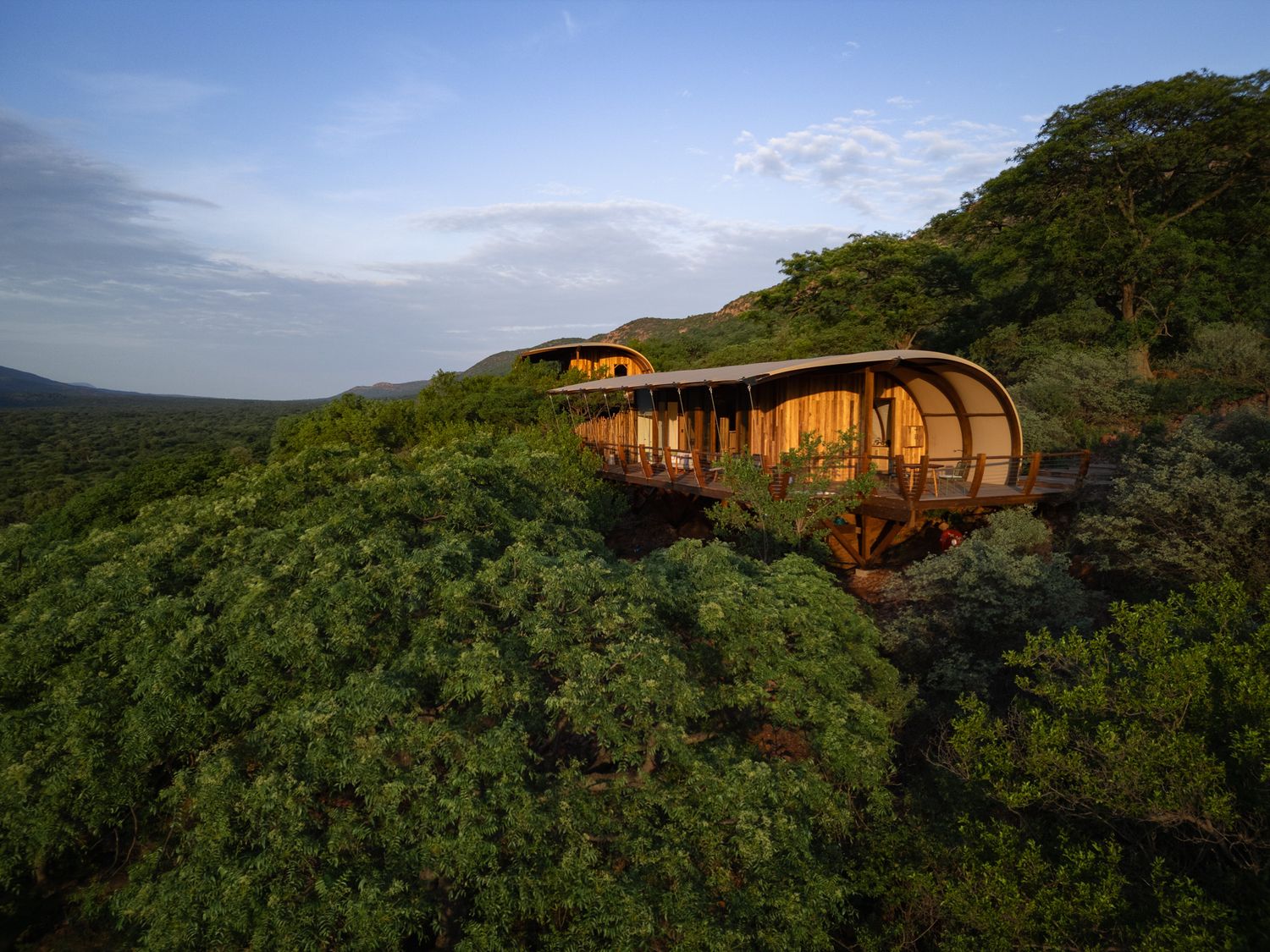Modern treehouse villa perched on hillside overlooking verdant valley at sunset.