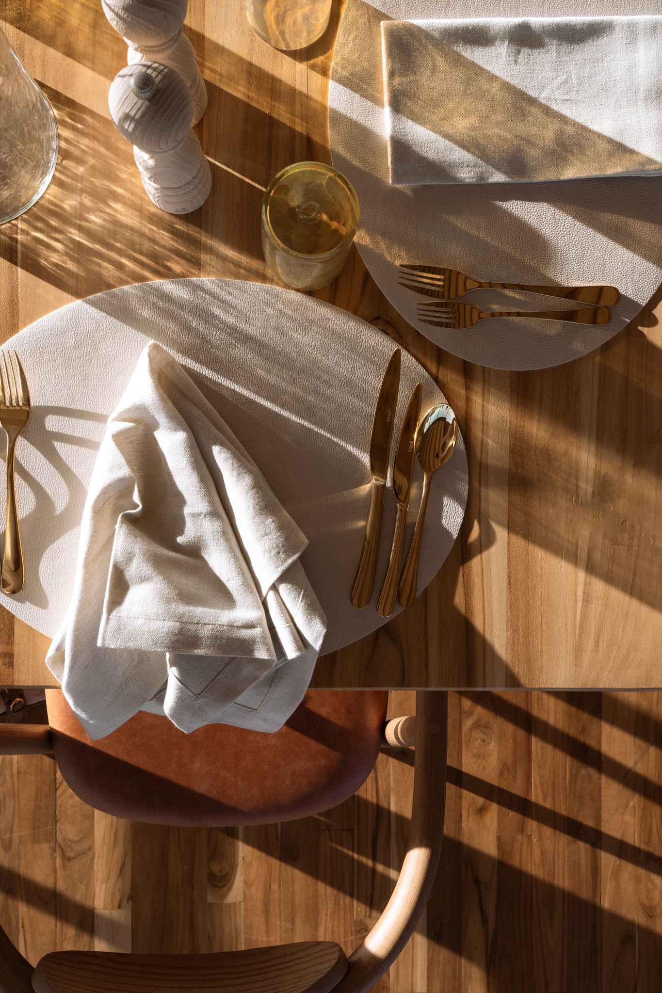 Place setting with white napkin and cutlery on wooden table in natural sunlight.