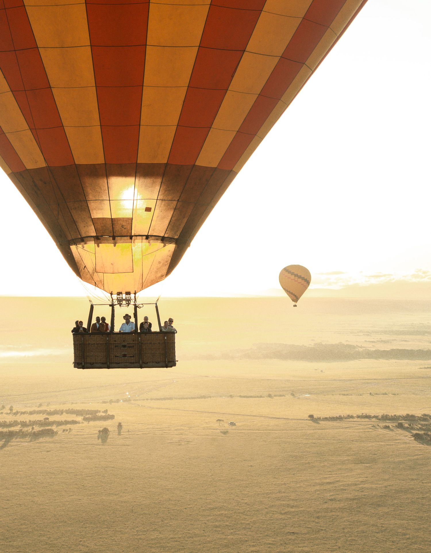 Hot air balloon with passengers floats above misty landscape at sunrise.