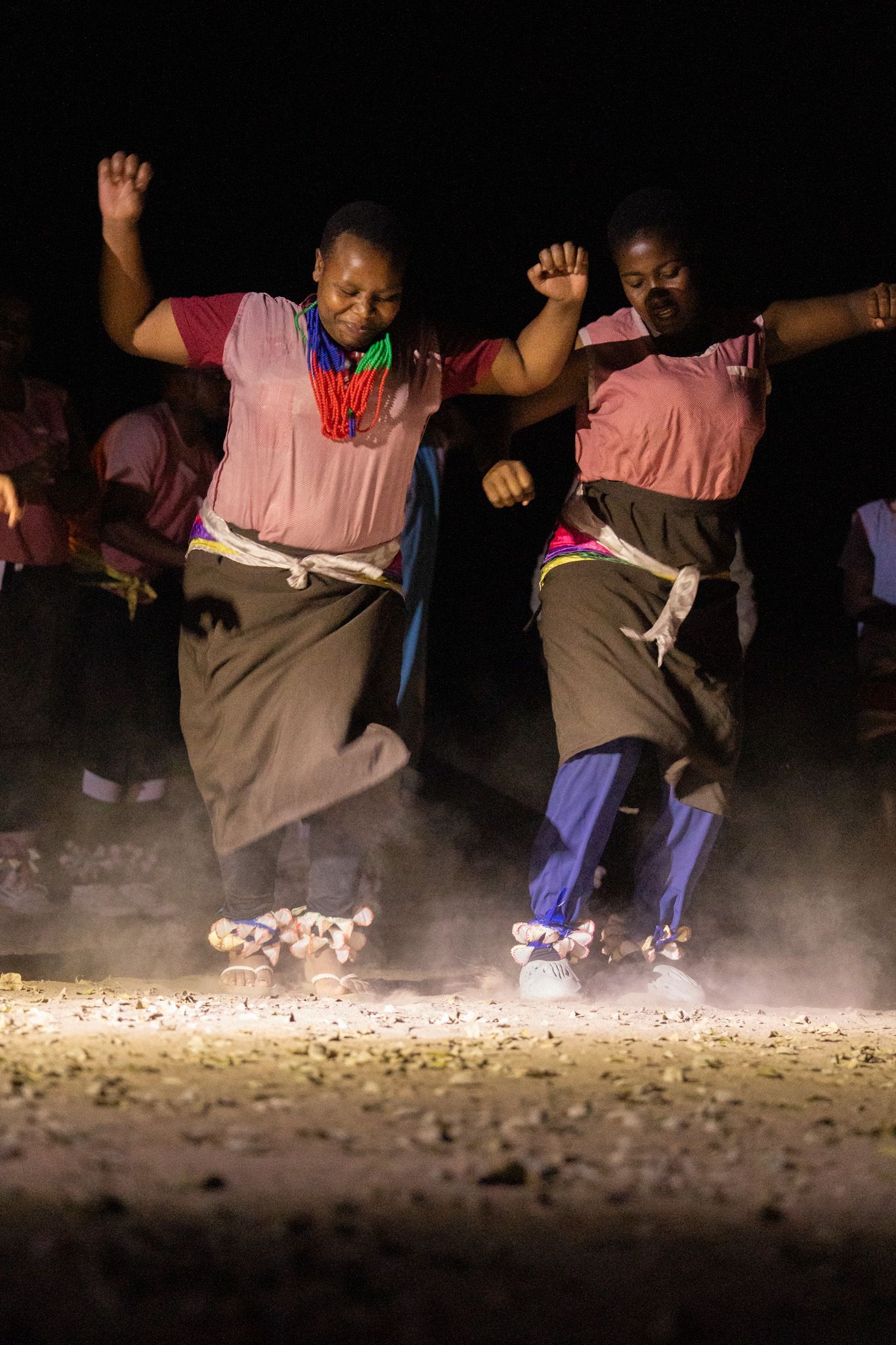 Dancers in pink tops performing synchronized jumps during a traditional dance performance.