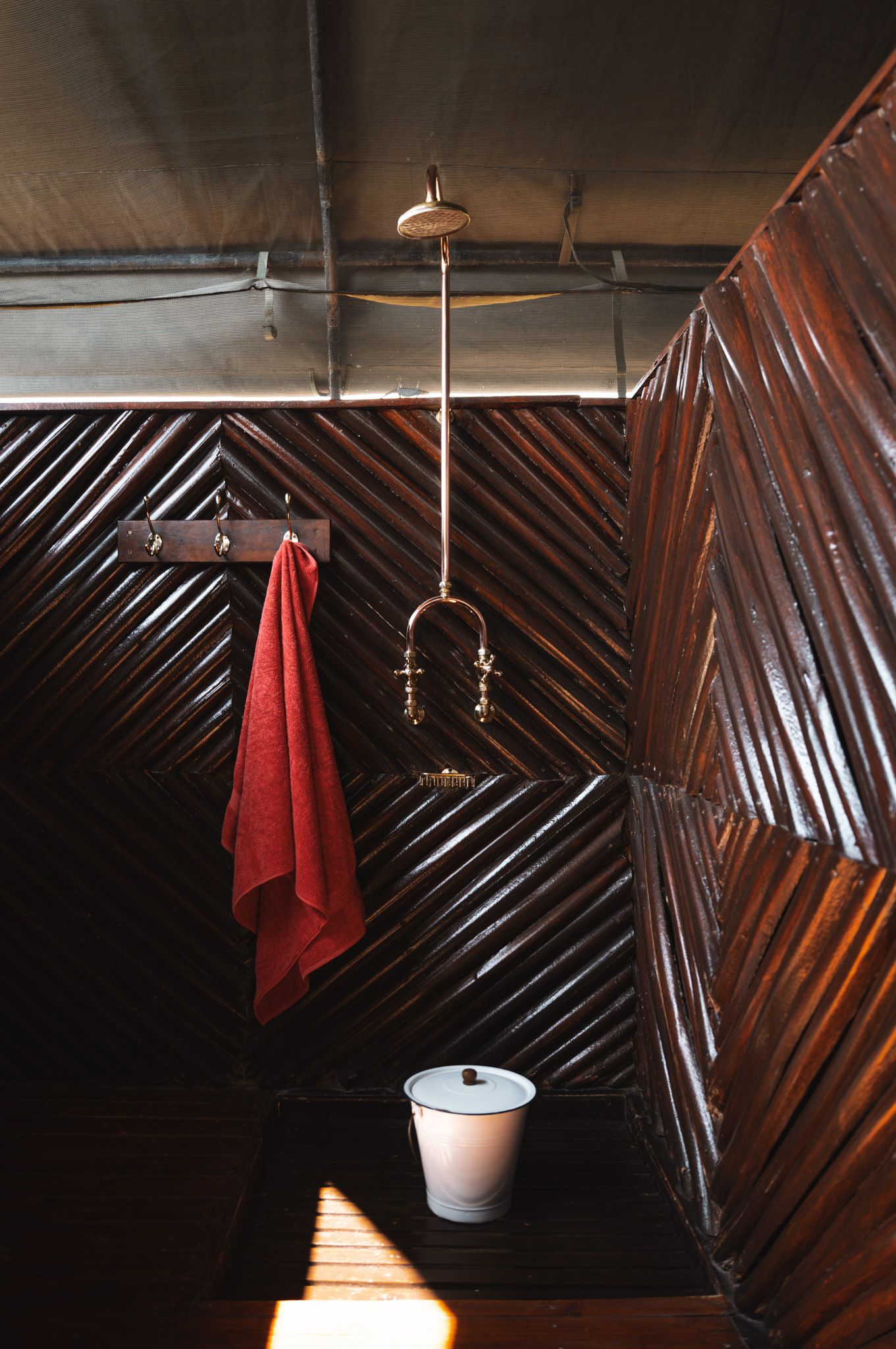 Dark wooden bathroom with diagonal paneling, hanging red towel, and pendant light fixture.