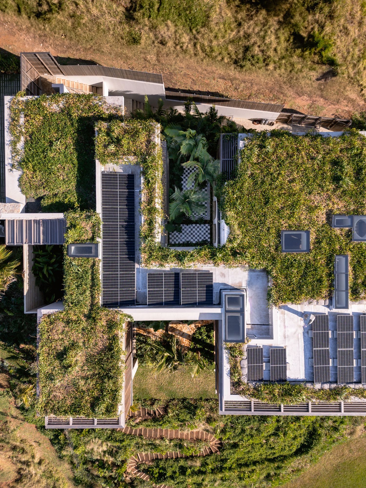 Modern house with solar panels on rooftop surrounded by lush vegetation viewed from above.