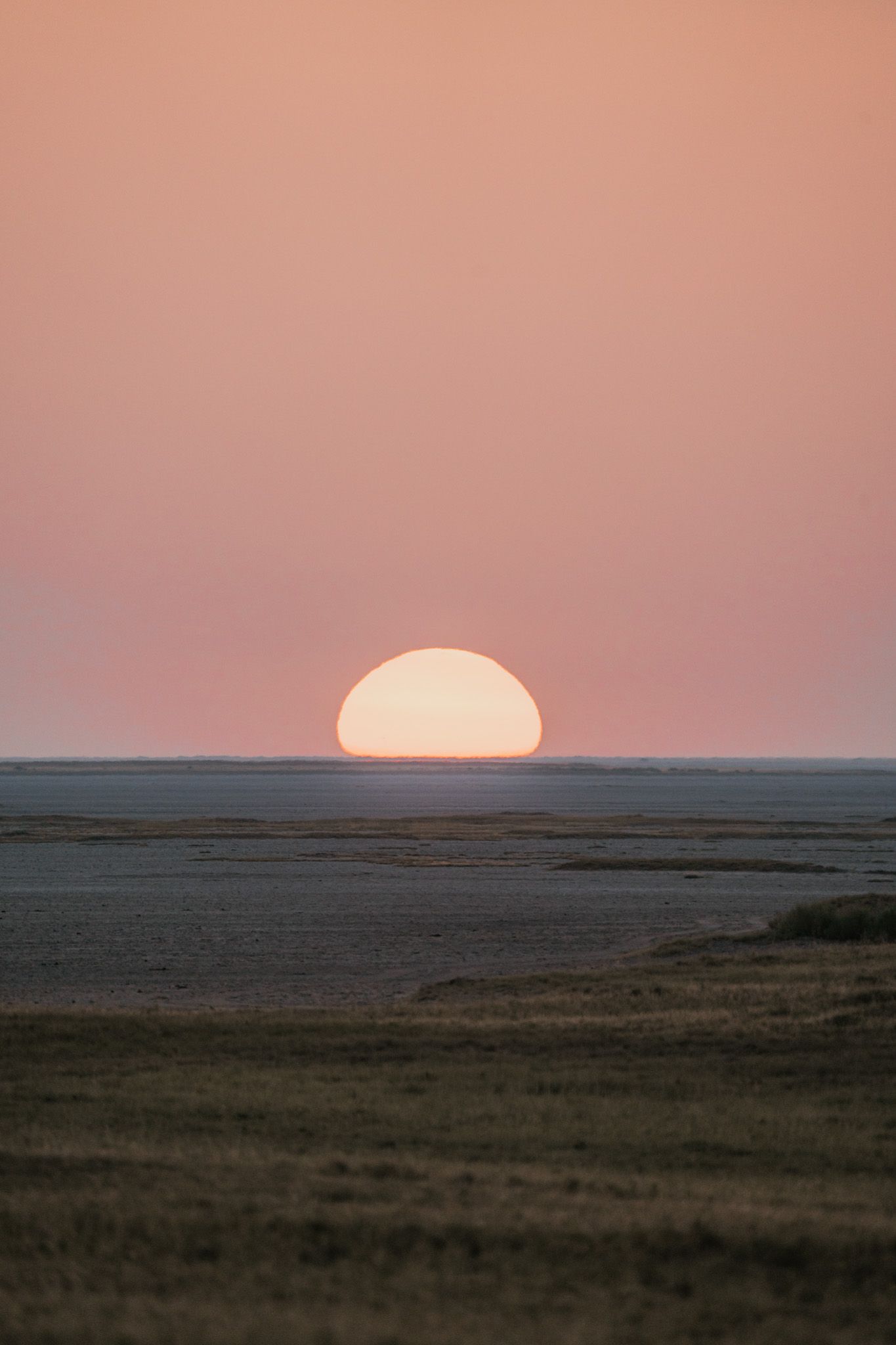 A large orange sun sets over a flat horizon creating a dramatic half-circle silhouette.