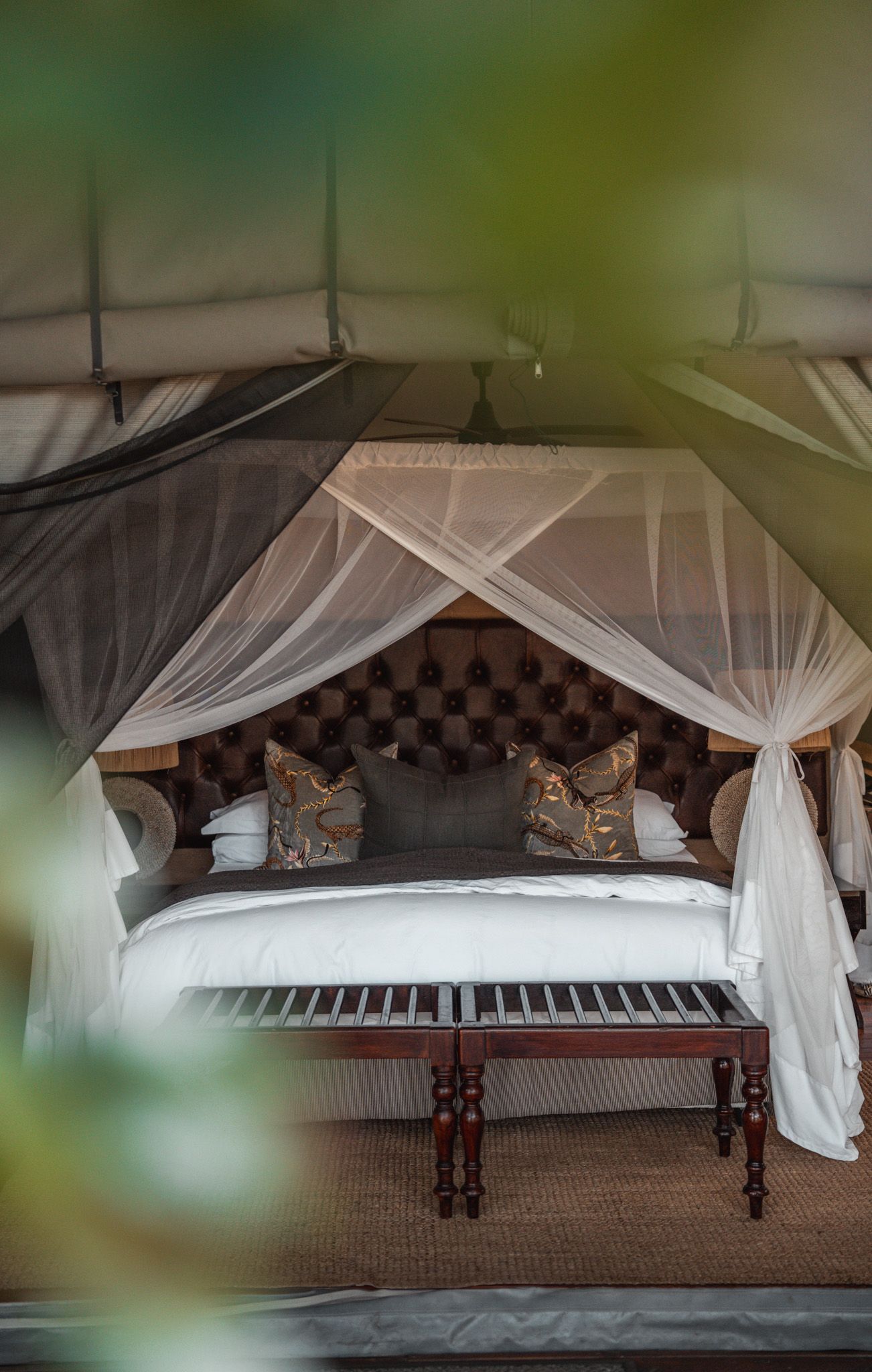 Luxury safari tent bedroom with mosquito netting and tufted headboard.