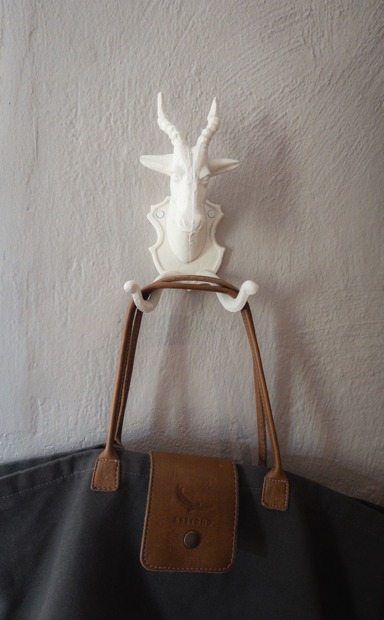 Minimalist white ceramic decorative piece mounted on brown leather straps against a textured wall.