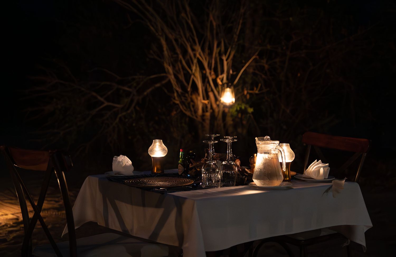 Elegantly lit outdoor dining tables set with glowing lanterns at dusk.