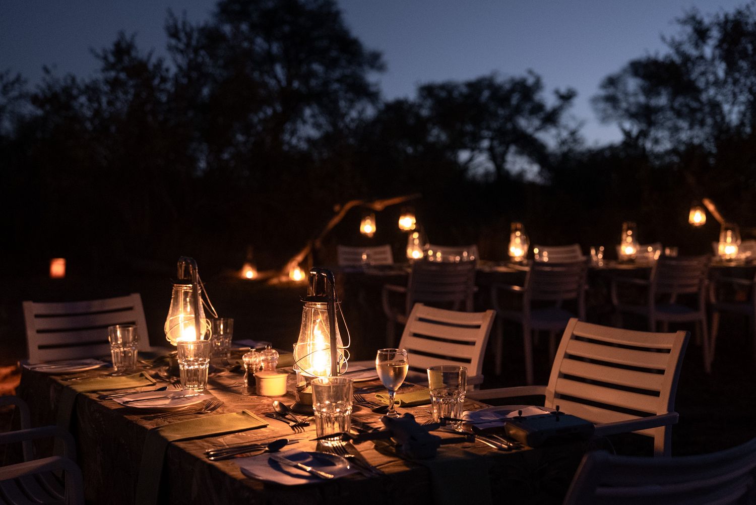 Candlelit outdoor dining setup with lanterns and wooden furniture at night.