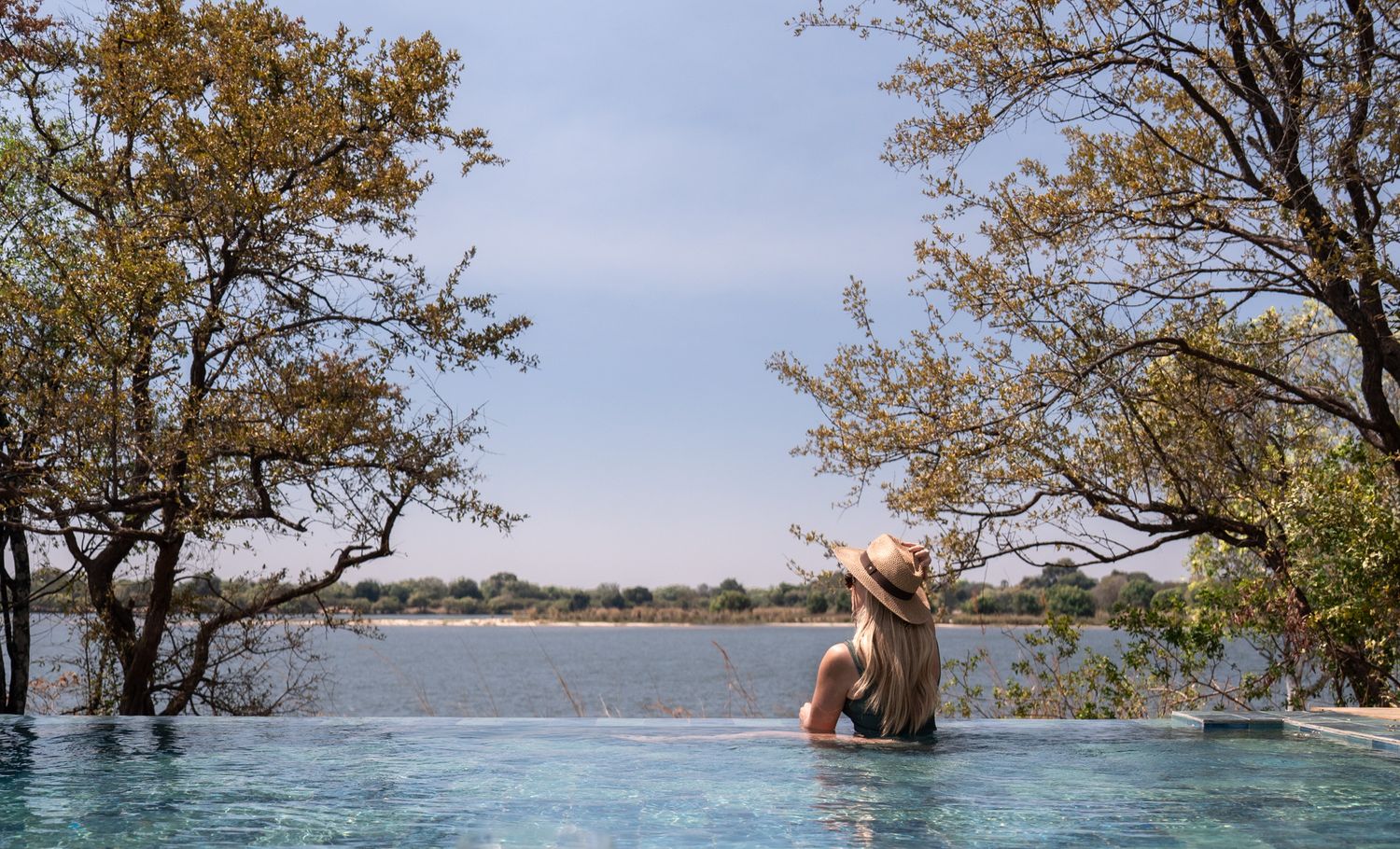 View of an infinity pool overlooking a serene lake with autumn trees framing the scene.