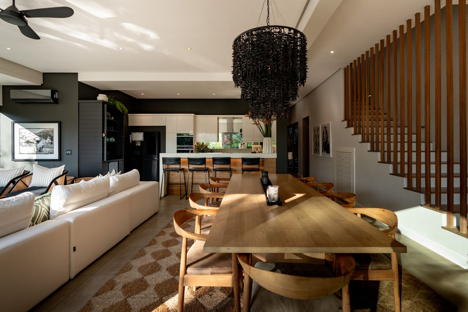 Modern open-concept living room with white sofa, wooden dining table, and dramatic black chandelier.