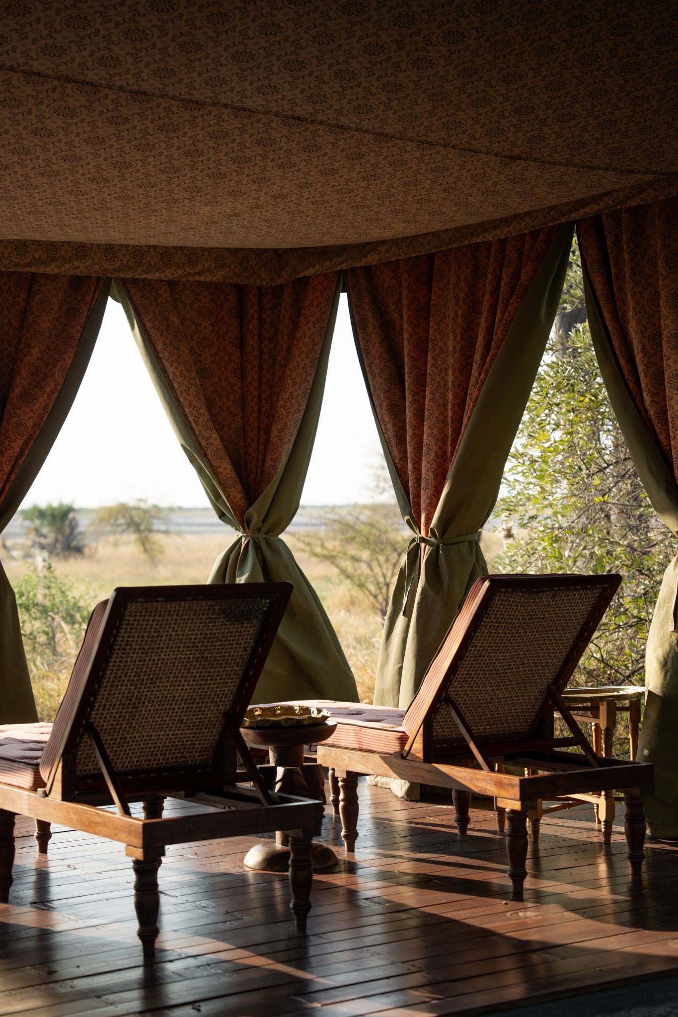 Safari lodge relaxation area with elegant chaise lounges and draped curtains offering savanna views.
