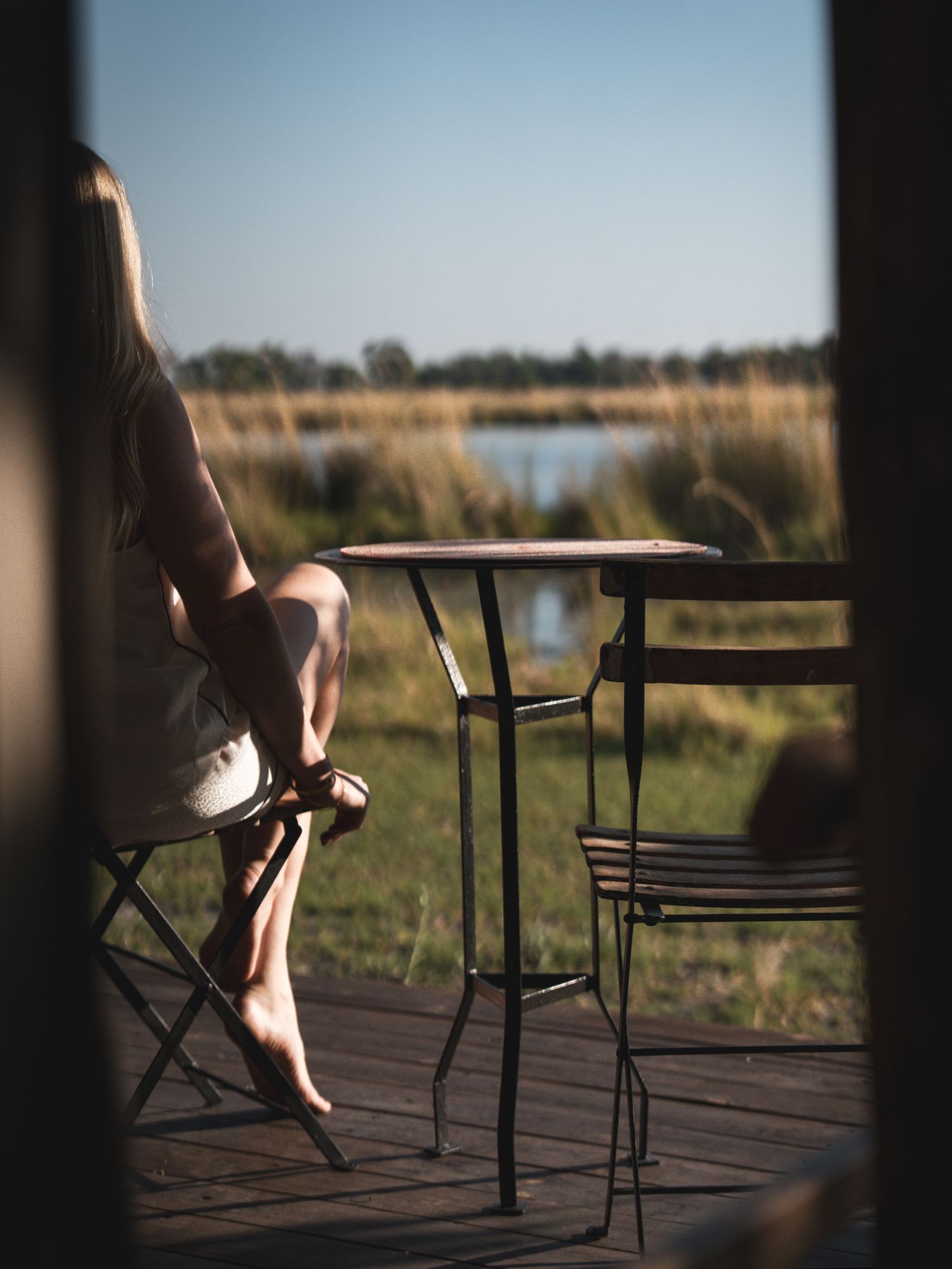 Silhouette of someone sitting on a deck chair overlooking a peaceful lake at sunset.